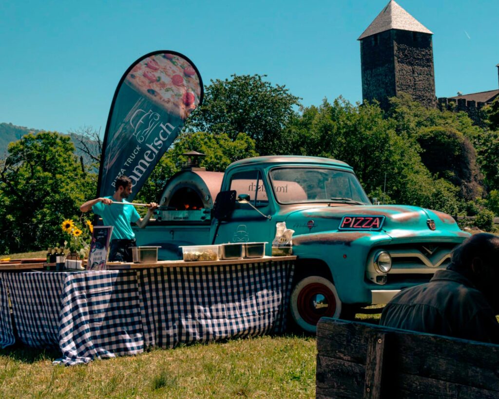 Ein Foodtruck mit Pizzaofen und sonnigem Biergarten. Vorbereitungen laufen.